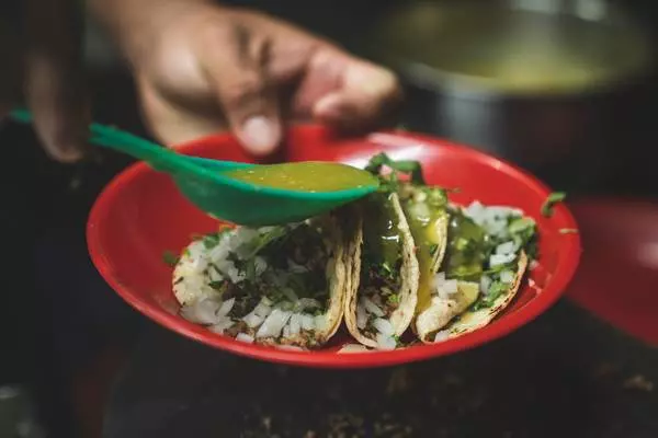 des tacos dans une assiette rouge et une personne versant de la sauce verte